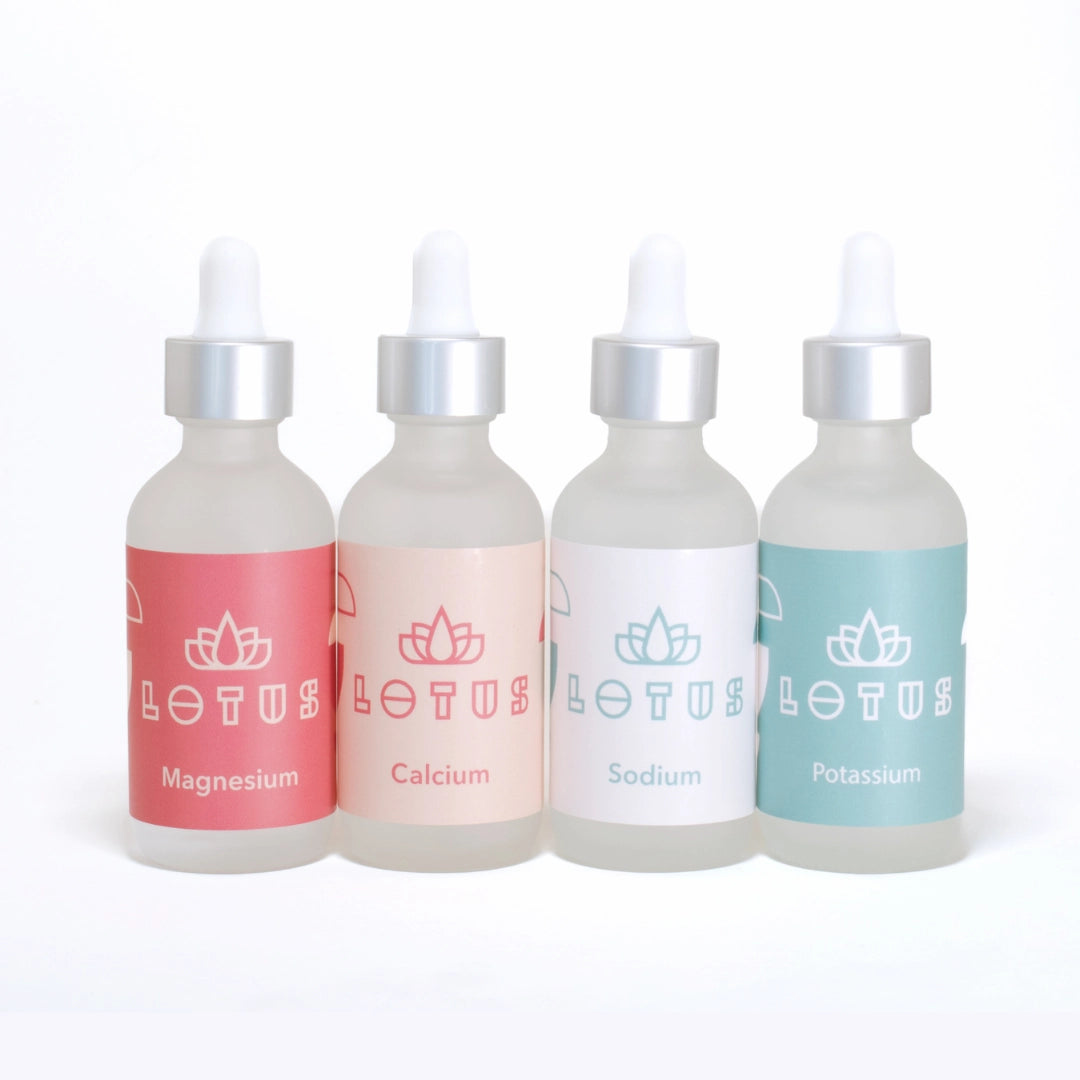 Set of 4 Lotus Water Mineral bottles with different coloured labels on a white background, Labeled: Magnesium, Calcium, Sodium, Potassium.