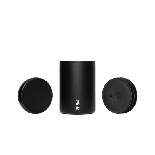 A matte black cylindrical insulated container with a matching lid and insert plunger, featuring the vertical white 'Miir' logo near the bottom, set against a plain white background.
Miir Airlock Coffee Storage Container