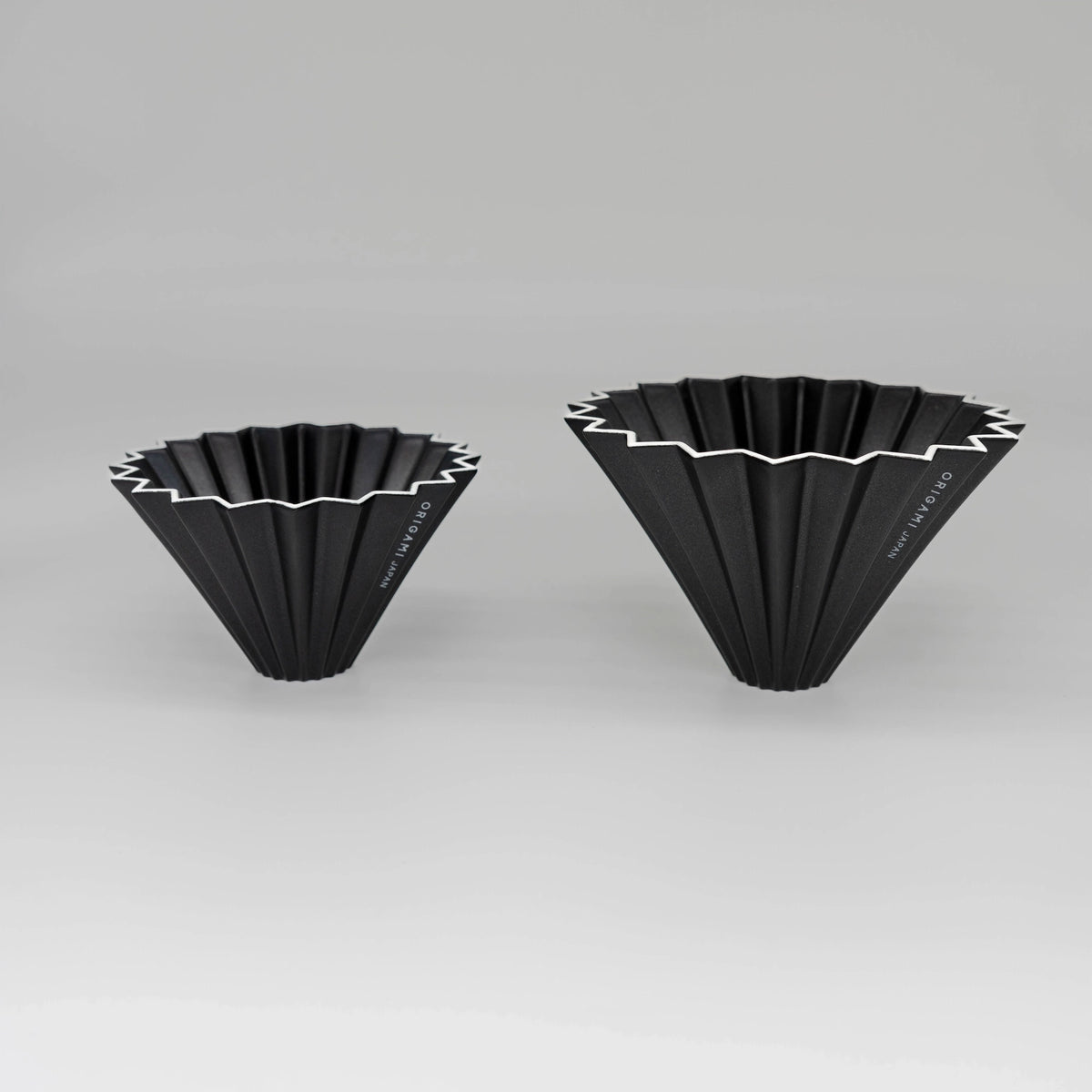 Two black pour over coffee drippers with white zigzag patterns flower dripper Origami coffee brewer on a white background