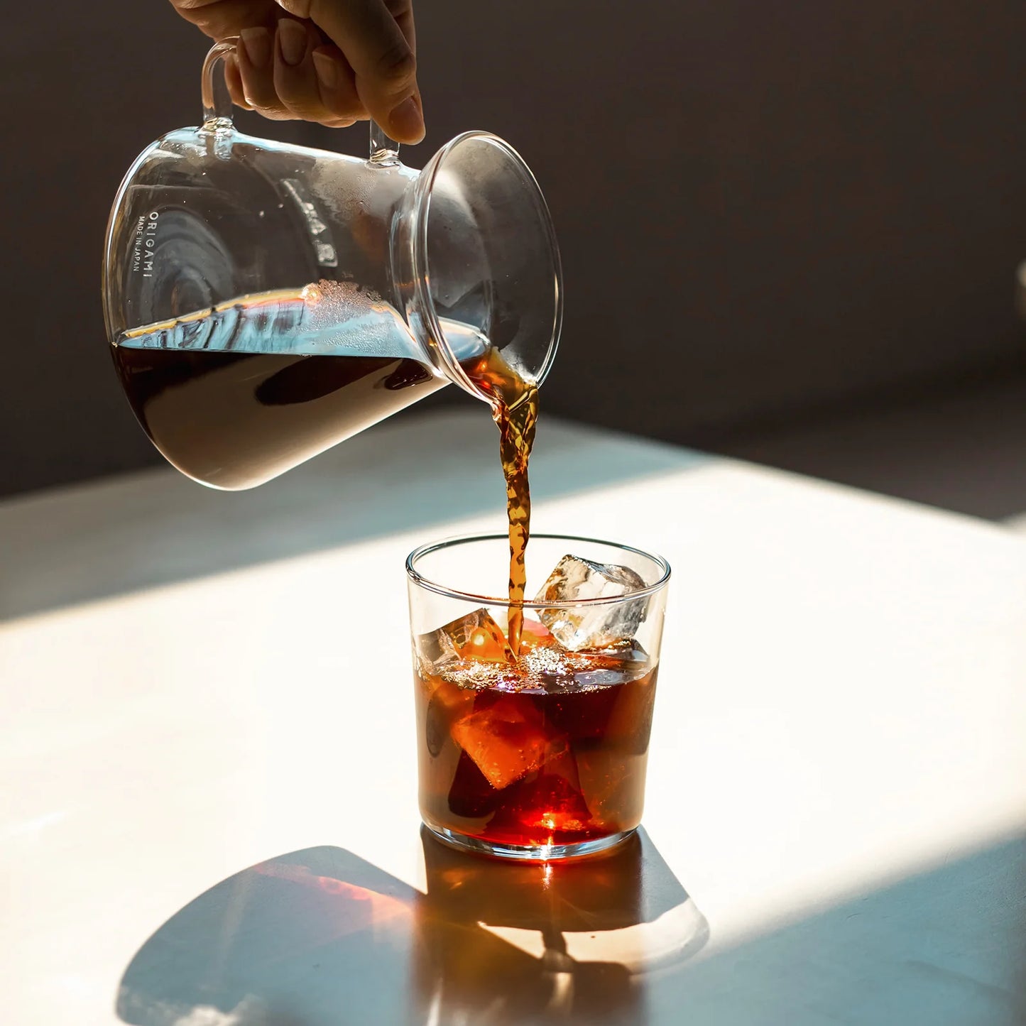 Origami and Hario Glass Coffee Server pouring pour over coffee over glass cup holding ice cubes. Basic Barista coffee Gear
