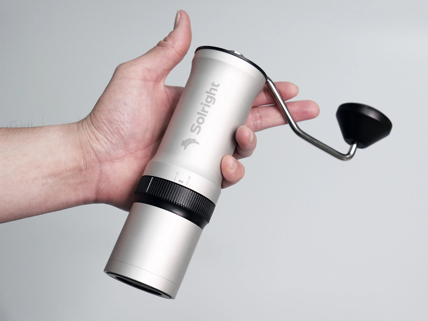 Hand holding a silver Solight coffee hand grinder against a gray background