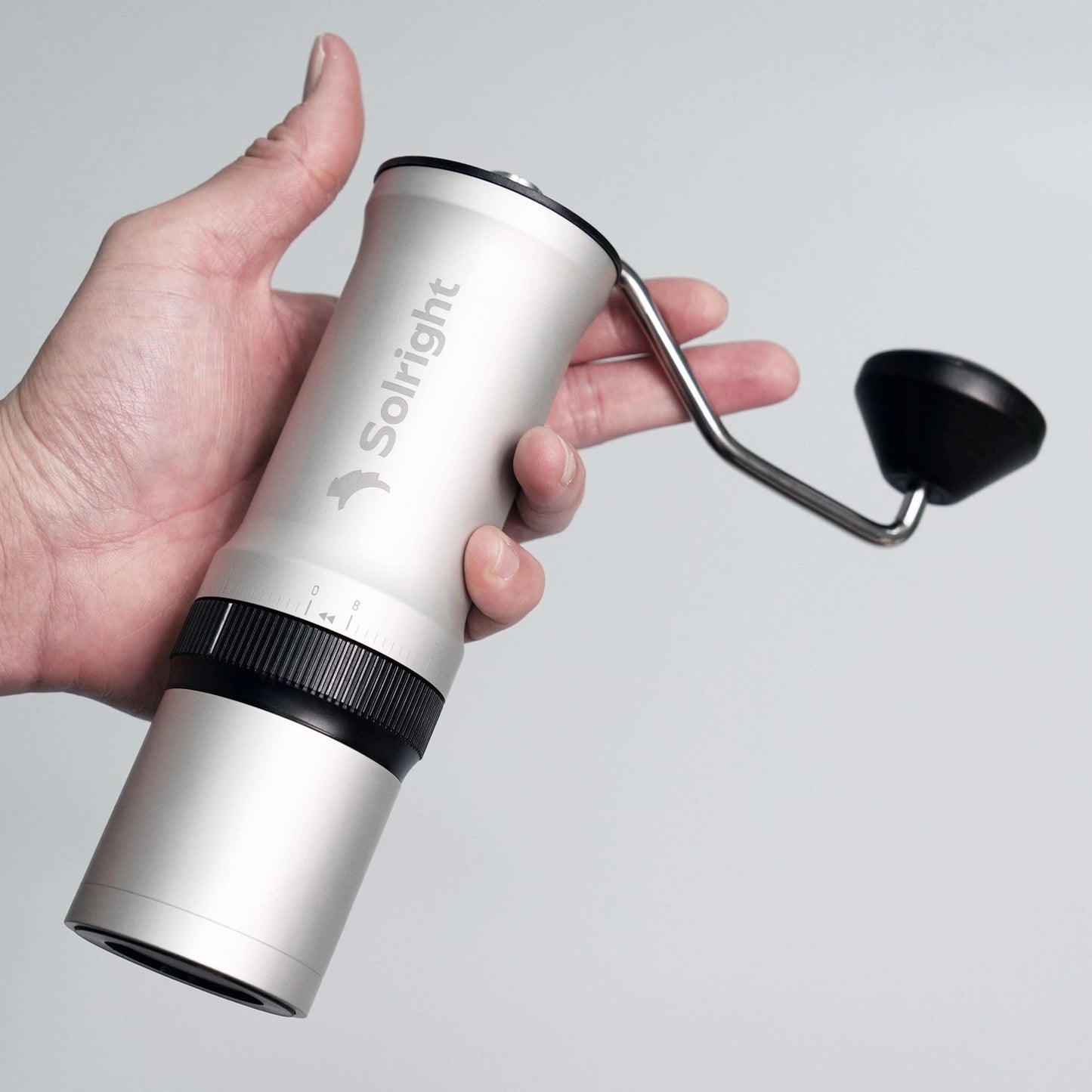 Hand holding a silver Solight coffee hand grinder against a gray background