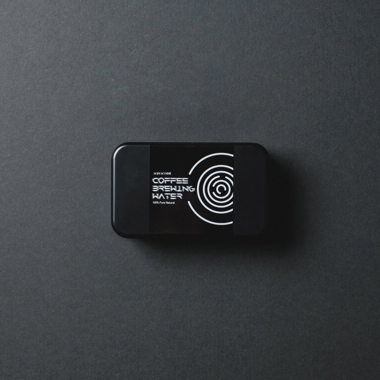 Black 'Aquacode' Tin of water brewing mineral sachets (liquid form) resting on black paper background with dark shadows - Basic Barista Product Image