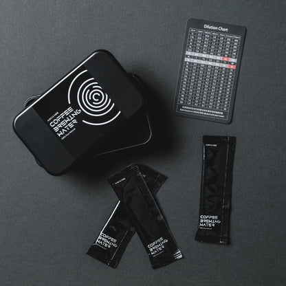 Black 'Aquacode' Tin of water brewing mineral sachets (liquid form) and dilution chart resting on black paper background with dark shadows - Basic Barista Product Image