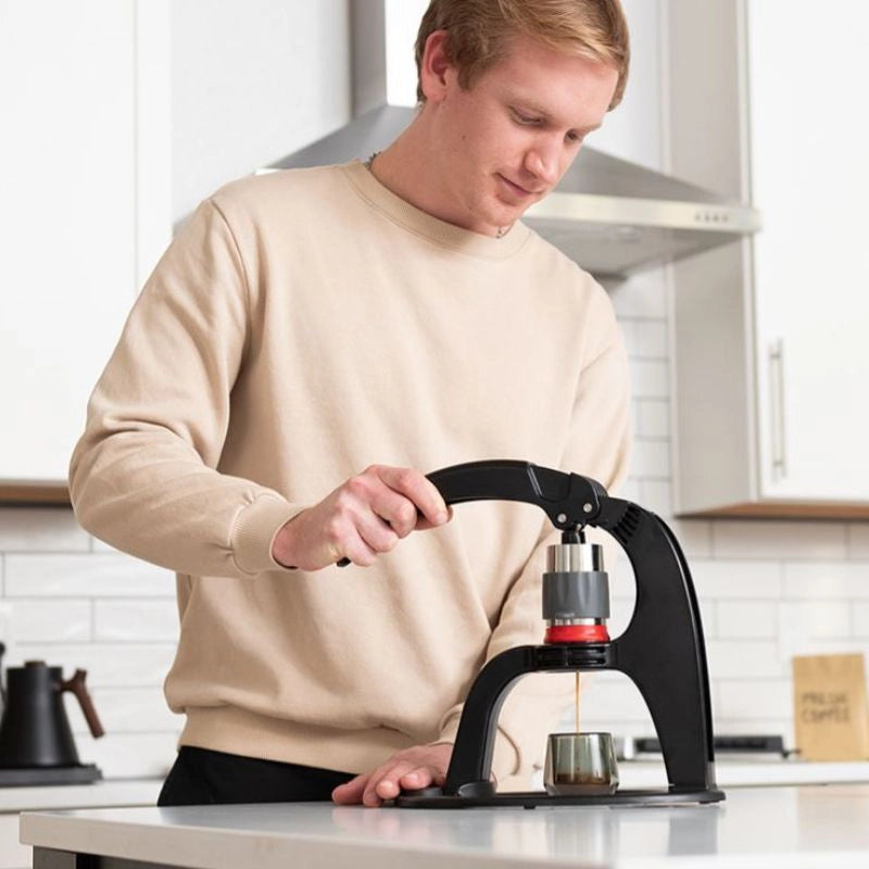 Person using a Flair Neo Flex Manual Espresso Maker in a white coloured, bright kitchen background. Pouring espresso shot into glass espresso cup
