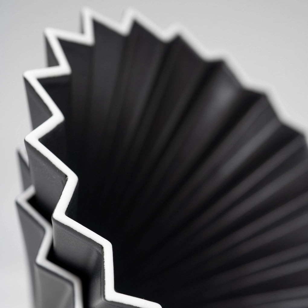 Close-up of a ceramic pour over origami matte black coffee dripper with white edge on white background