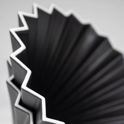 Close-up of a ceramic pour over origami matte black coffee dripper with white edge on white background