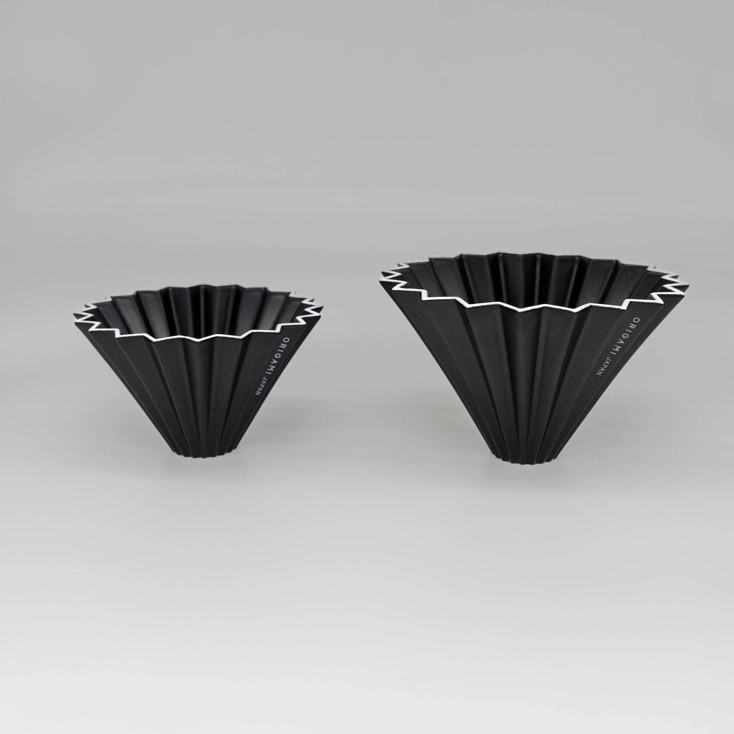 Two black pour over coffee drippers with white zigzag patterns flower dripper Origami coffee brewer on a white background