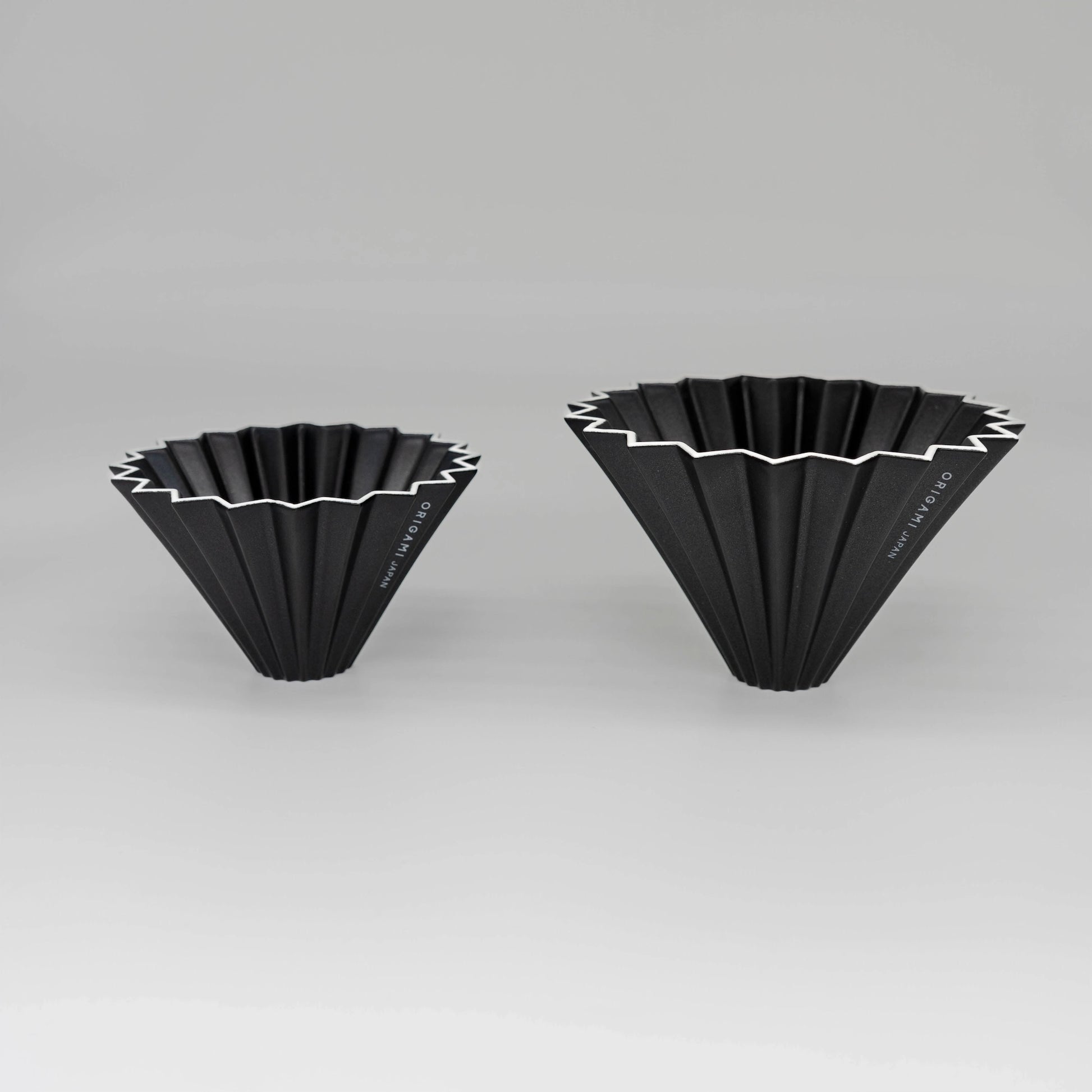 Two black pour over coffee drippers with white zigzag patterns flower dripper Origami coffee brewer on a white background