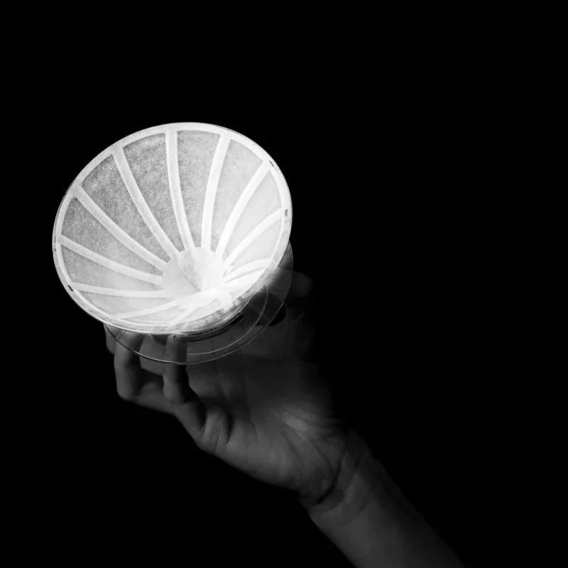 Hand holding a UFO Dripper with the Sibarist filter paper inside Basic Barista Sibarist and UFO Filter Collaboration on black background