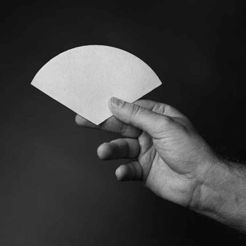 Hand holding a white sibarist UFO coffee filter paper against a black background - Basic Barist pour over coffee gear online
