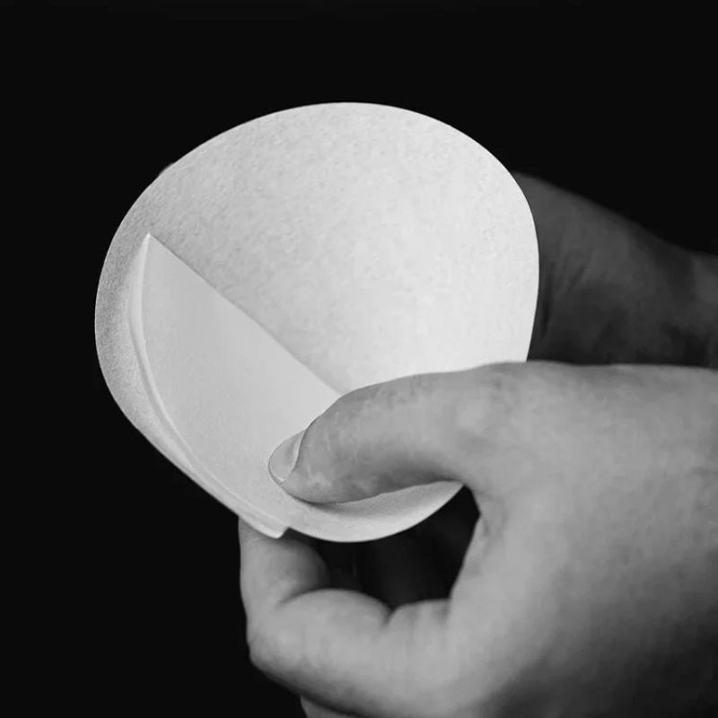 Hand holding a white round cone filter - Sibarist Pour Over coffee filters against a black background