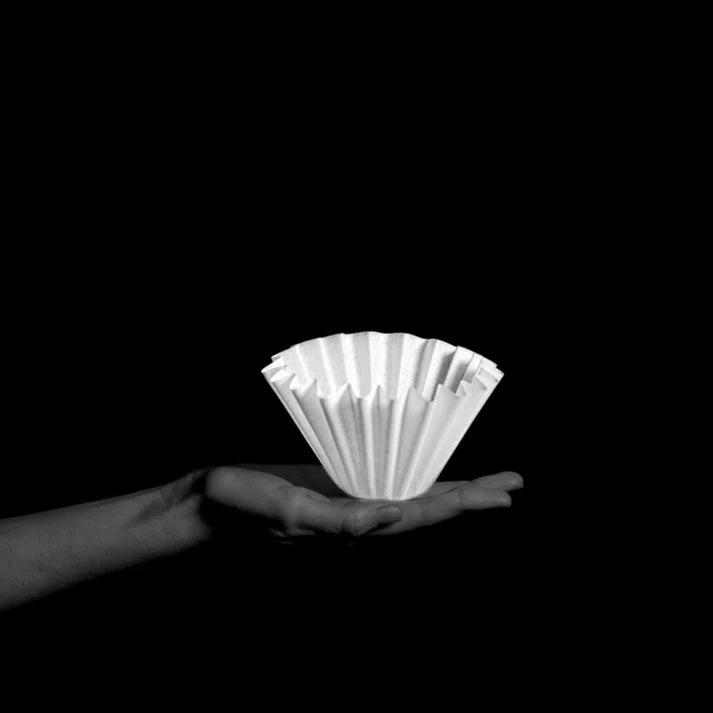 Hand holding a stack of white coffee filters - Sibarist Wave Filter Papers against a black background