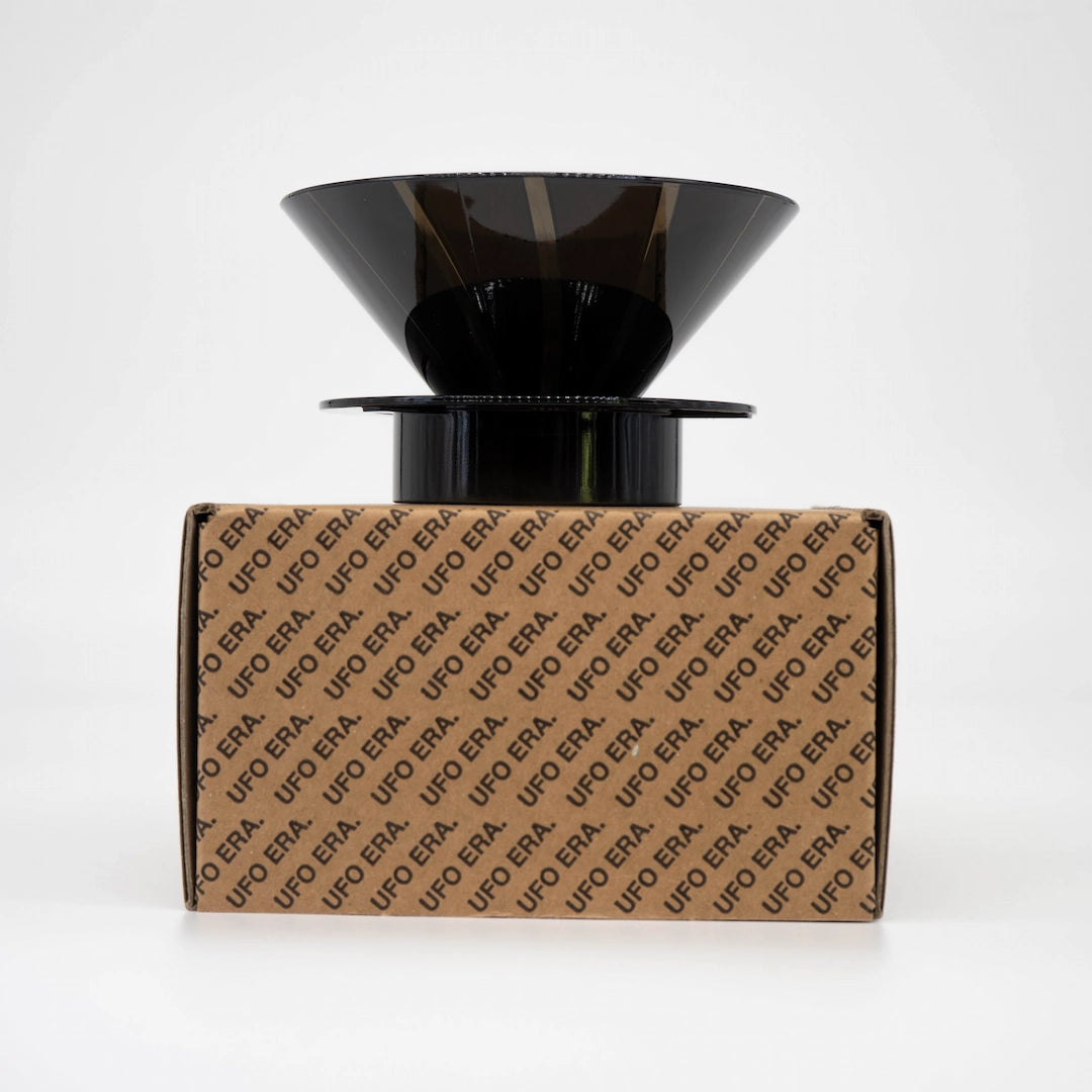 Black plastic UFO Dripper sitting on top of retail box (Front view) on a white background Basic Barista Pour Over Coffee Gear