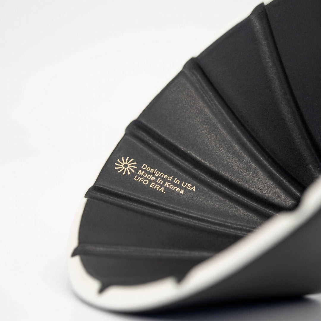 UFO Dripper Ceramic Matte Black Pour Over Coffee Dripper close up of logo: "Designed in USA Meade In Korea UFO ERA." 
on white background Basic Barista Coffee Gear Online